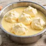 Leche de Pájaro: copos esponjosos de clara montada cocidos sobre crema de leche amarilla en un cuenco metálico