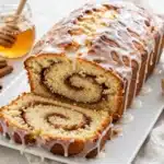 Pastel de Pan de Canela y Miel: pan dulce en forma de barra con remolino de canela y glaseado blanco, con una rebanada gruesa delante